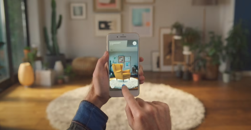 A person uses the IKEA augmented reality app on their phone to place yellow chair over a white rug in their home