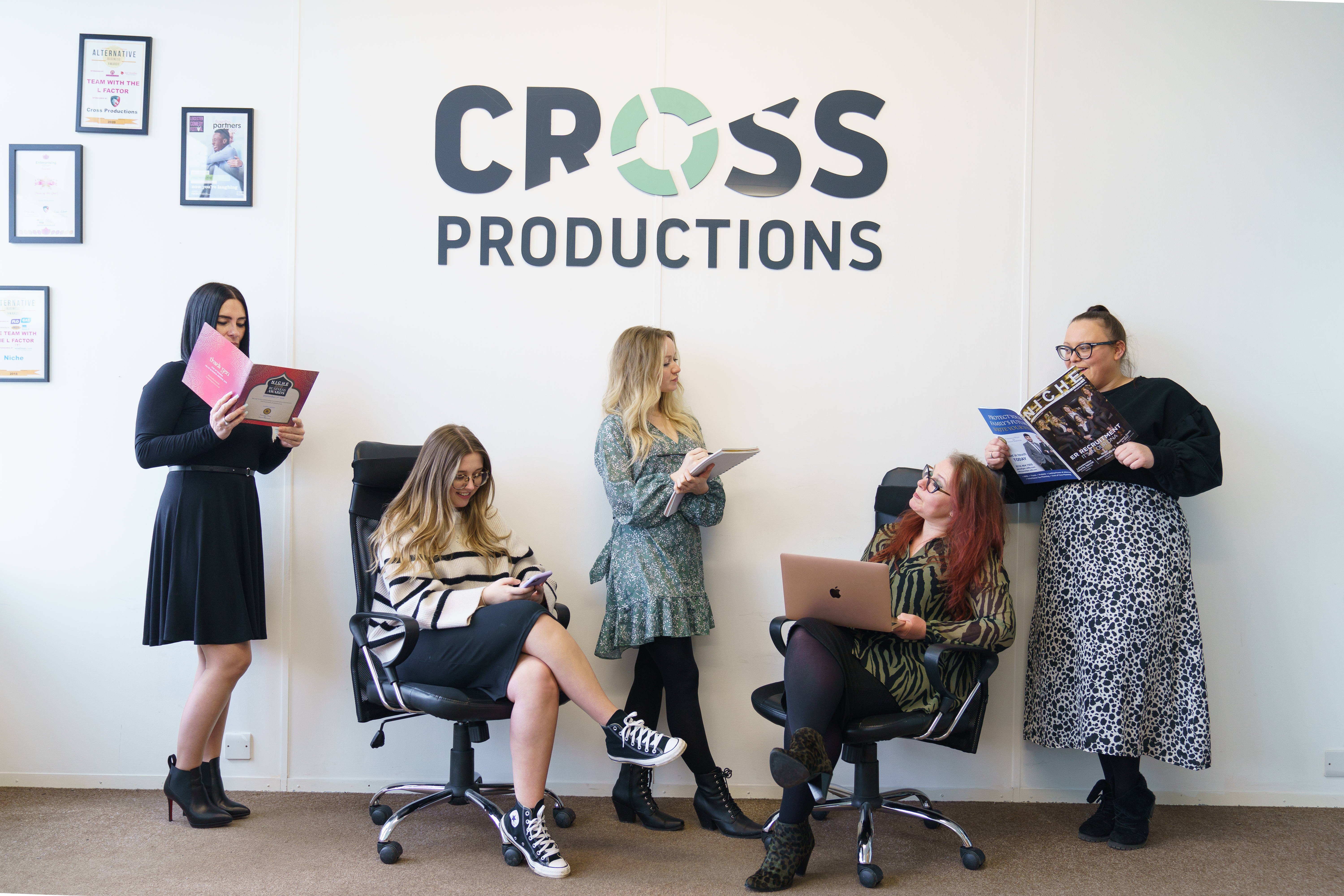 Cross Productions team members stand under a branded sign, reading magazines, and taking notes for blogging
