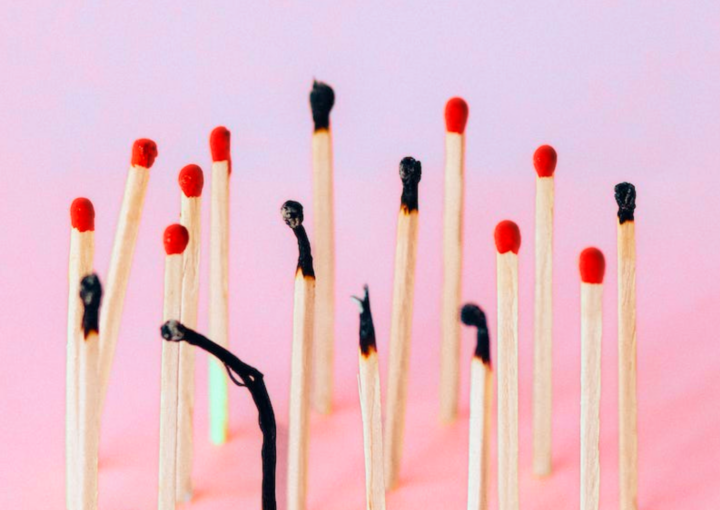 Business owner burnout: a pink and purple background with 17 matches standing up, one of them is burnout out and is completely black, some are only black at the tip, and others haven't been lit yet.