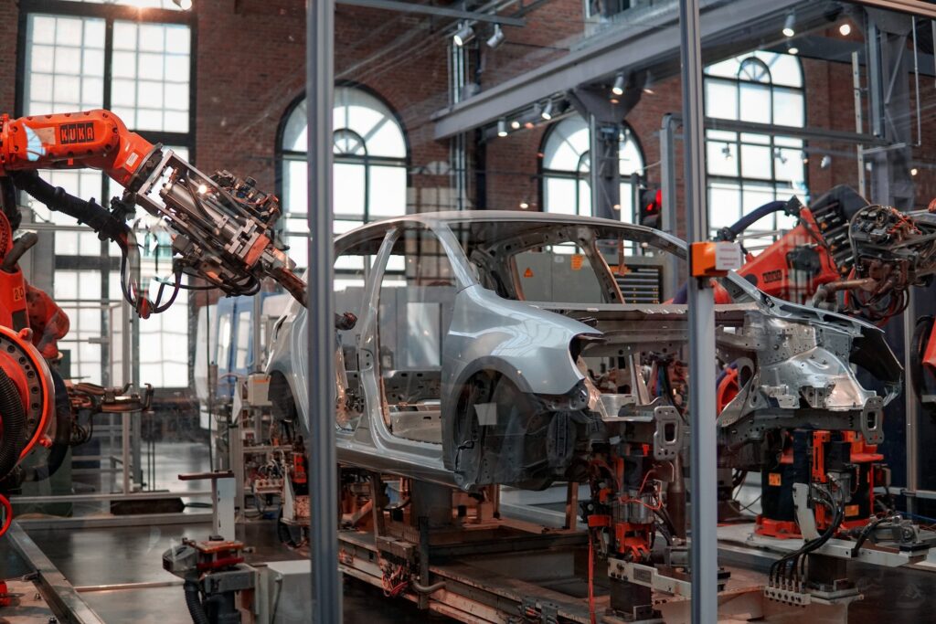 orange robots put together the silver frame of a car in a factory