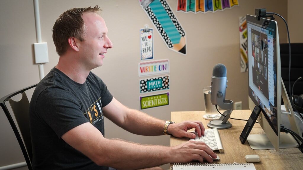 A smiling man conducting a professional webinar on a Mac with a microphone