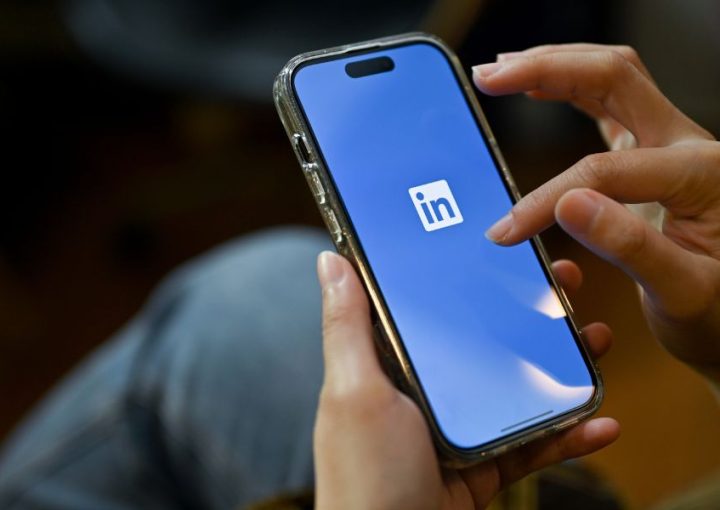 Two hands holding a mobile phone with a blue background and LinkedIn logo on the screen