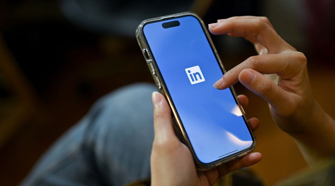 Two hands holding a mobile phone with a blue background and LinkedIn logo on the screen